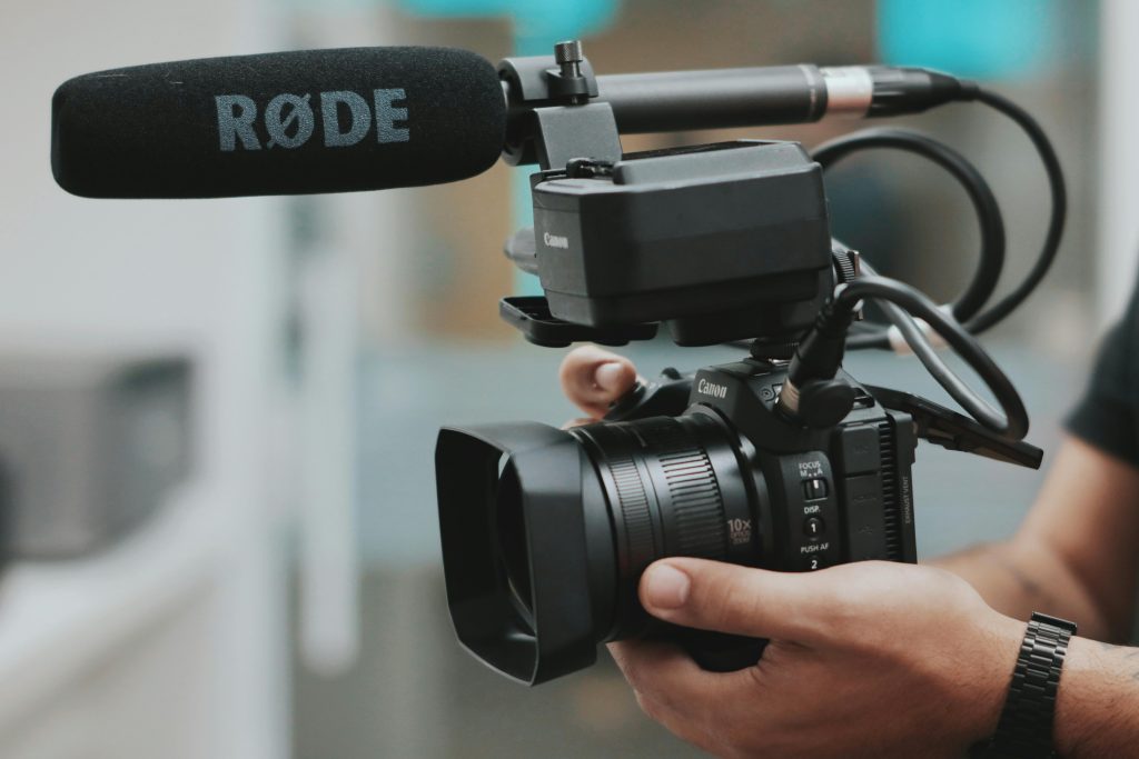 pexels photo 2170450 2170450 Close-up of hands holding a professional video camera with a RØDE microphone attached.