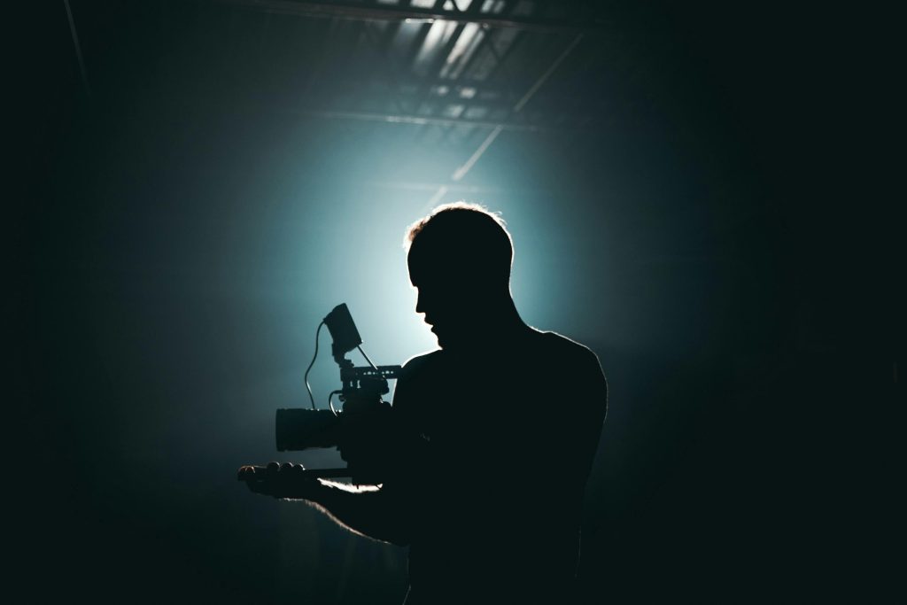 pexels photo 3379934 3379934 Silhouette of a cinematographer with camera gear in a dramatic, low light setting.