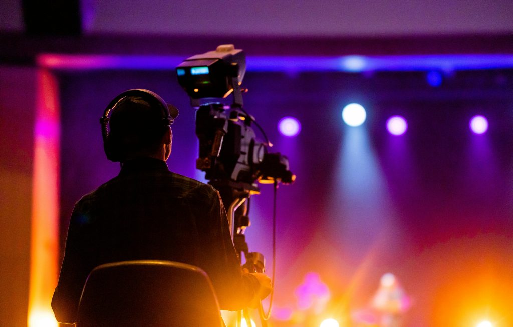 pexels photo 9618875 9618875 A videographer recording a live concert with vibrant spotlights, using professional equipment.